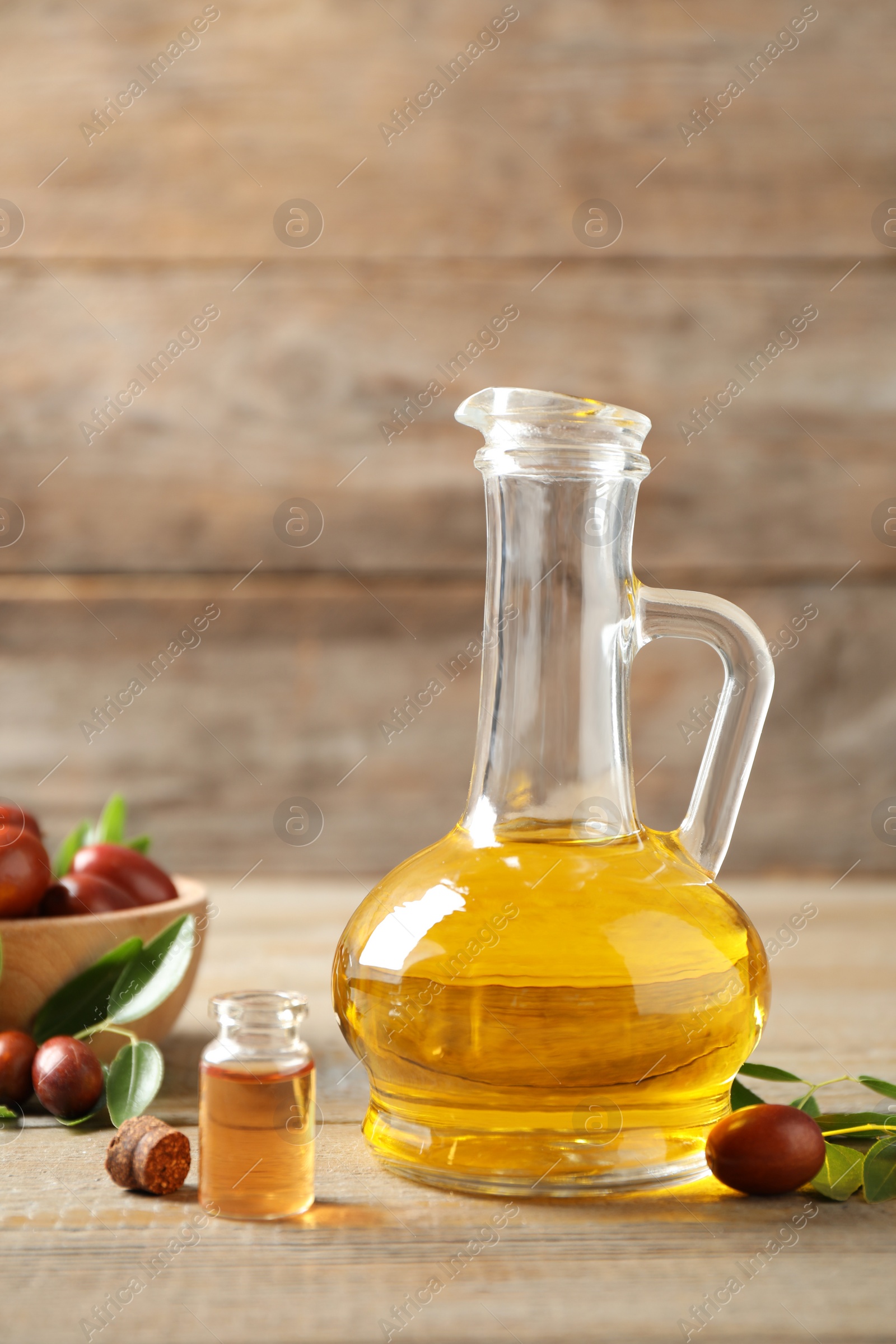 Photo of Glass jug with jojoba oil and seeds on wooden table