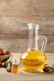 Glass jug with jojoba oil and seeds on wooden table