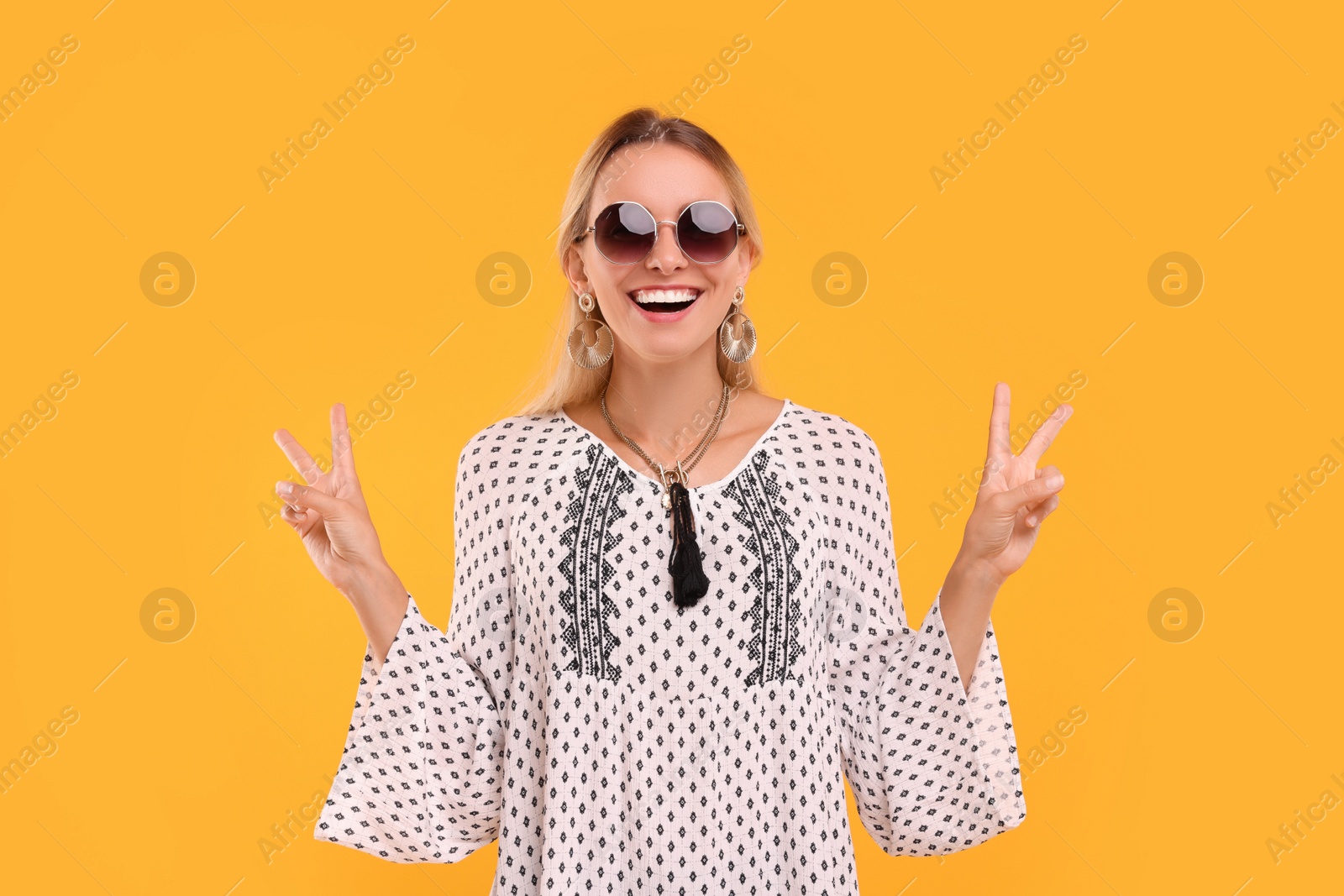Photo of Portrait of smiling hippie woman showing peace signs on yellow background