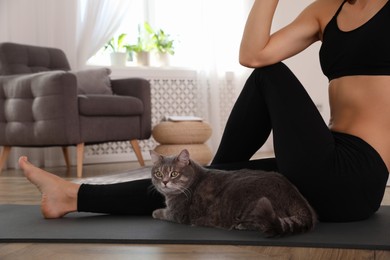 Photo of Beautiful woman practicing yoga near her cat at home, closeup