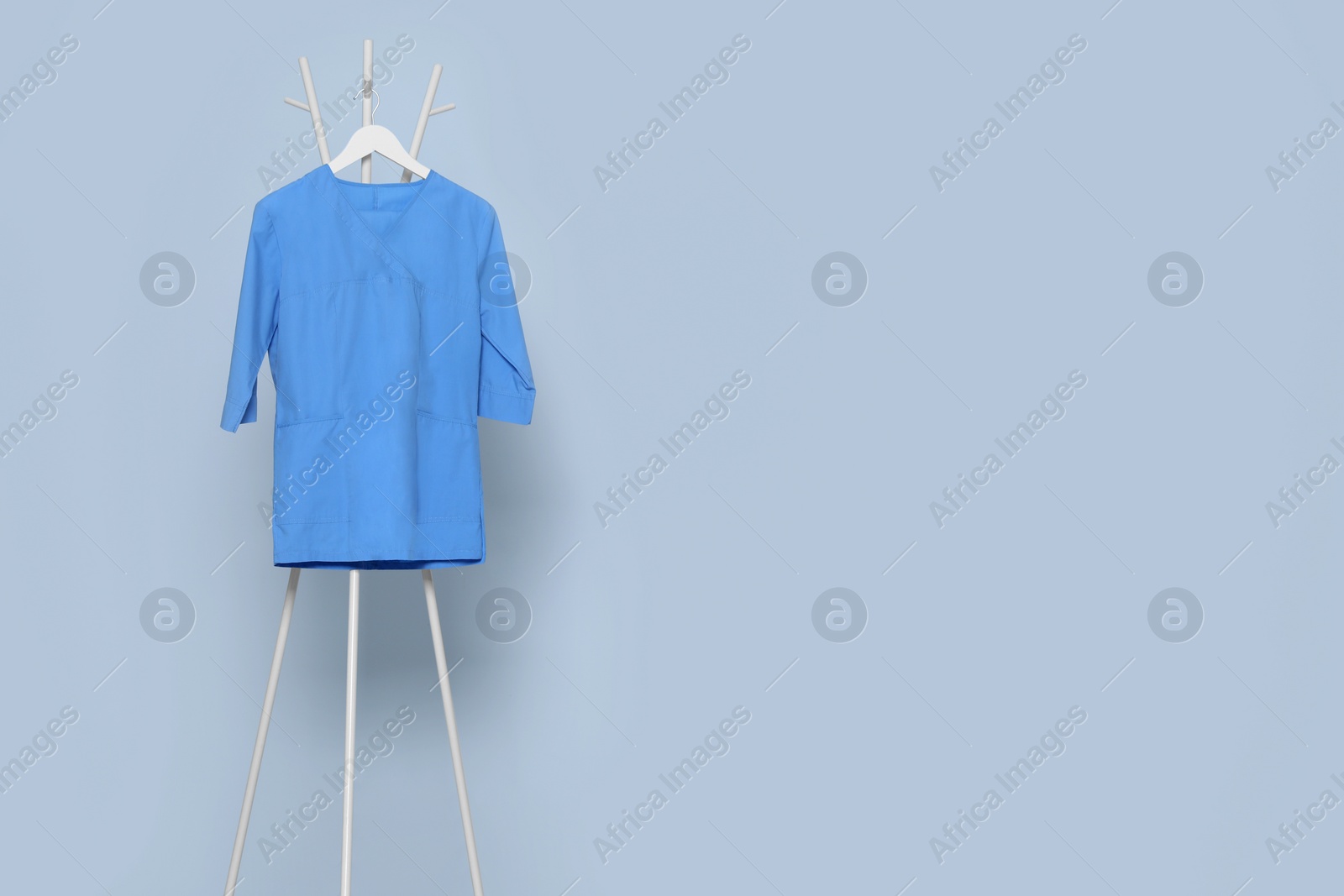 Photo of Blue medical uniform hanging on rack near light grey wall indoors. Space for text