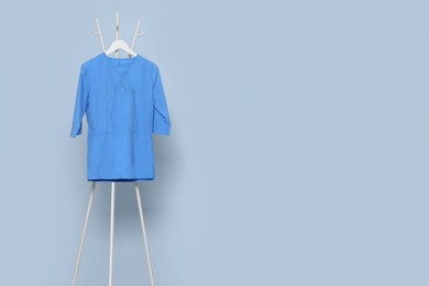 Photo of Blue medical uniform hanging on rack near light grey wall indoors. Space for text