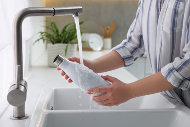 Woman washing thermo bottle in kitchen, closeup