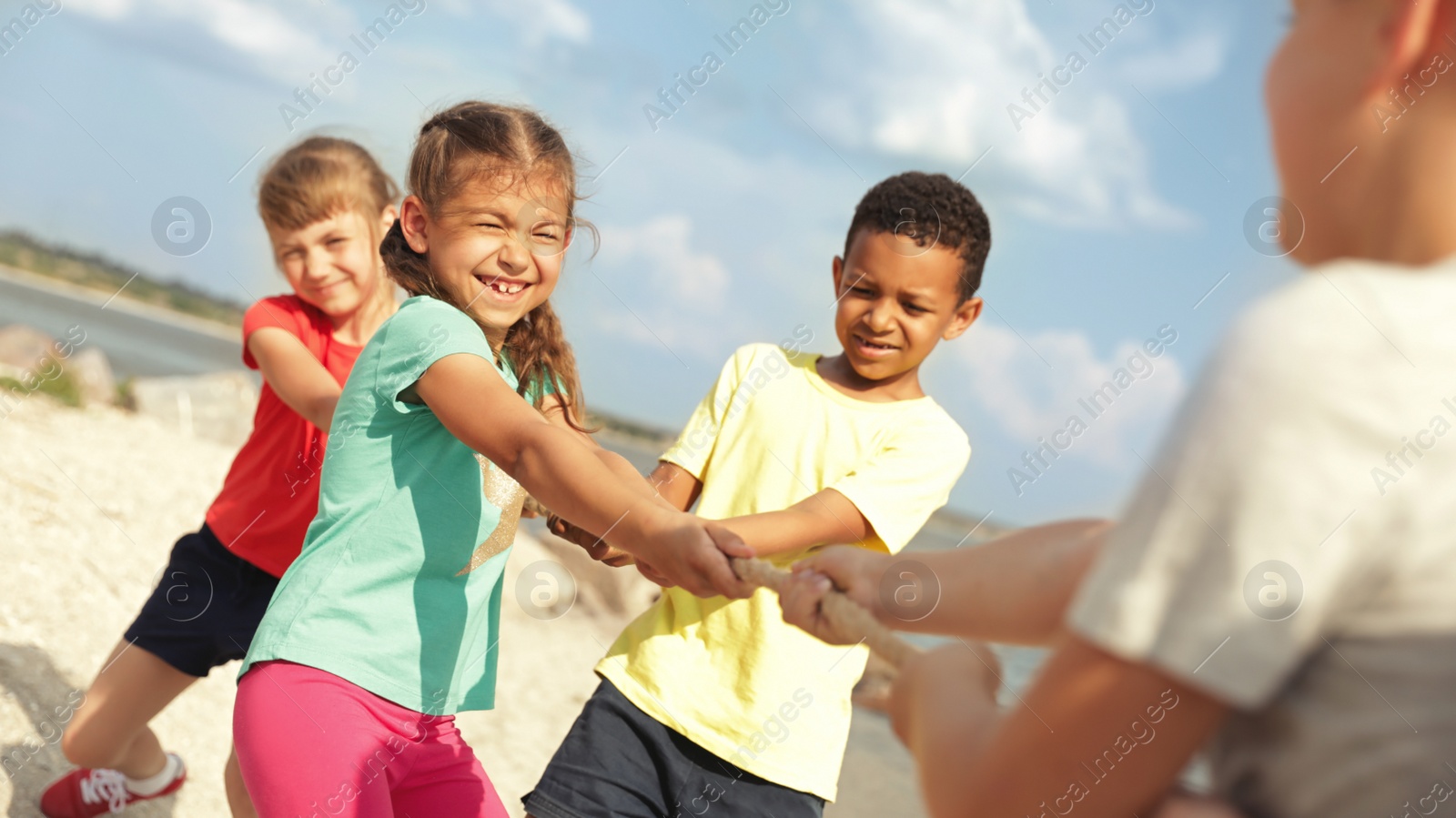 Image of Cute little children playing tug of war game outdoors on sunny day