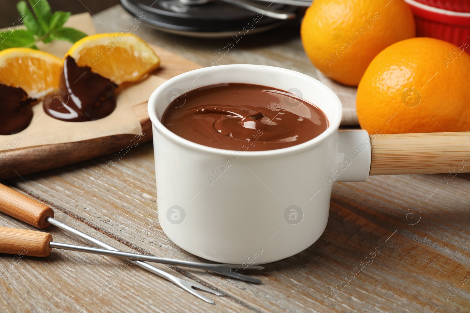 Photo of Fondue pot with milk chocolate and oranges on wooden table, closeup