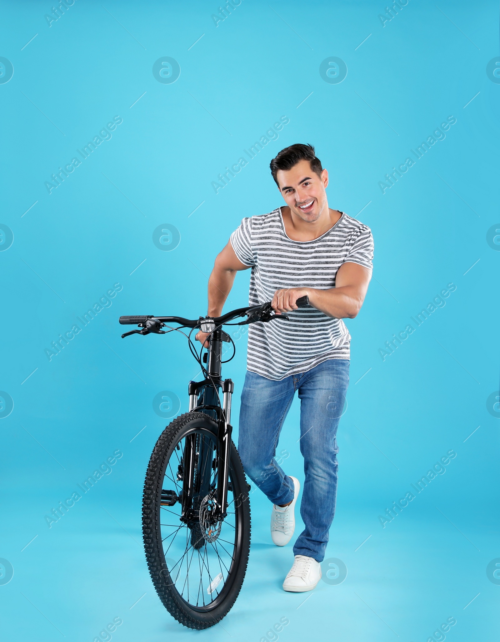 Photo of Handsome young man with modern bicycle on light blue background