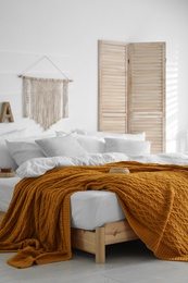 Photo of Comfortable bed with warm knitted plaid in stylish room interior