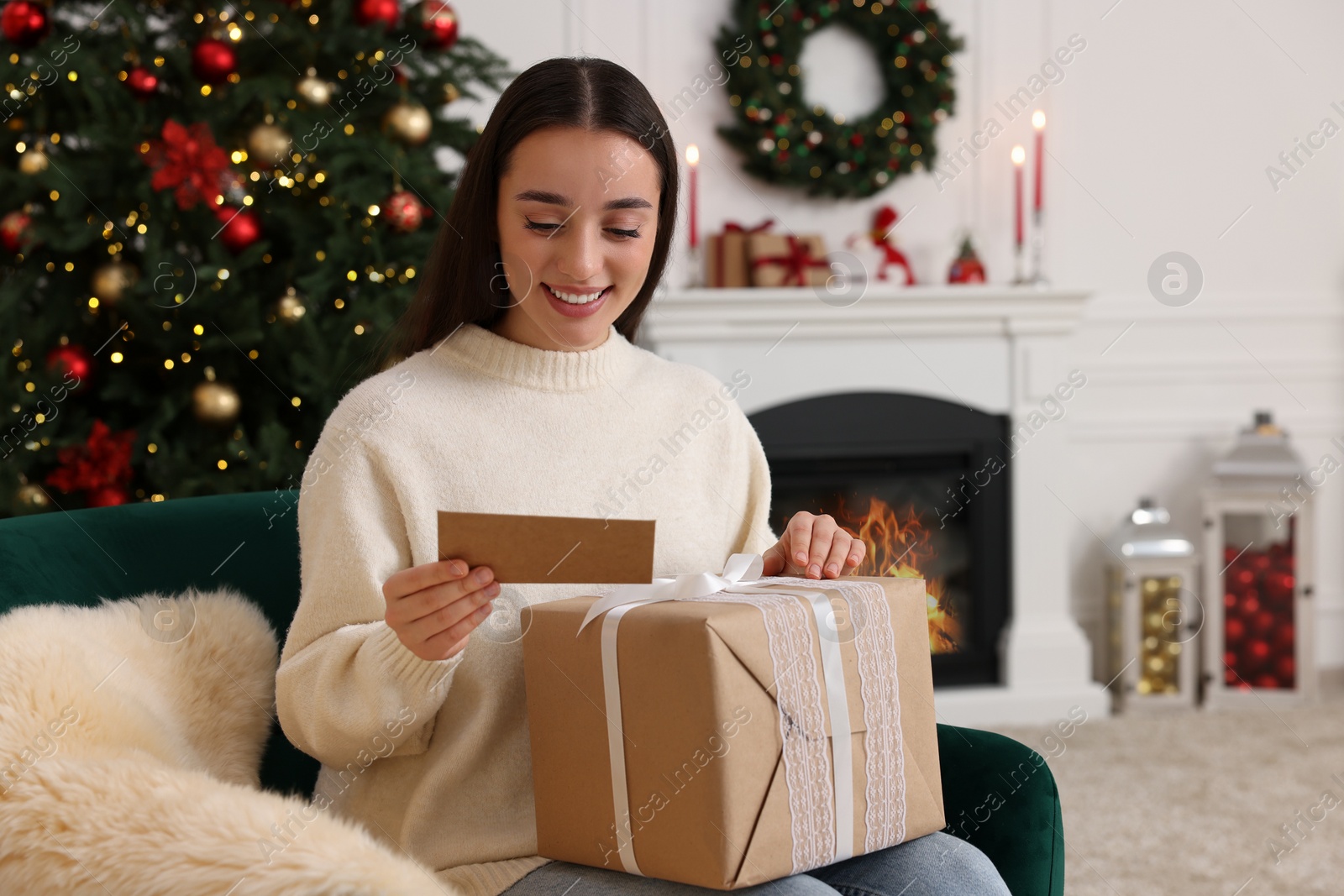 Photo of Happy young woman with Christmas gift reading greeting card at home