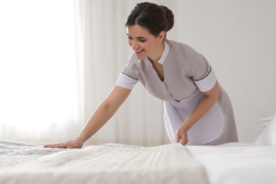Photo of Young maid making bed in hotel room