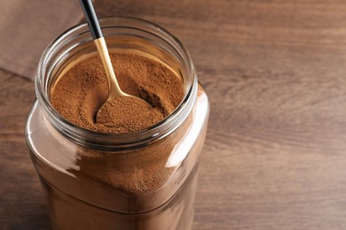 Photo of Jar of instant coffee and spoon on wooden table, closeup. Space for text