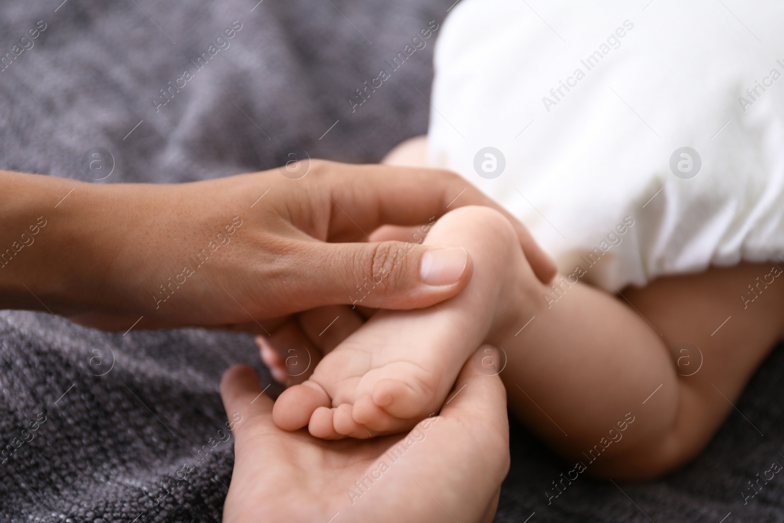 Photo of Woman massaging cute little baby on blanket, closeup