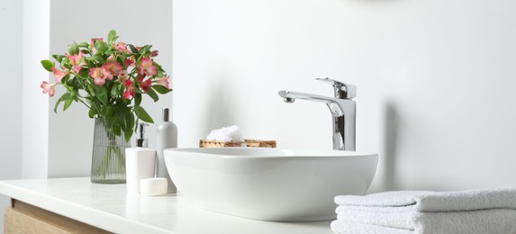 Photo of Vase with beautiful Alstroemeria flowers and toiletries near sink in bathroom