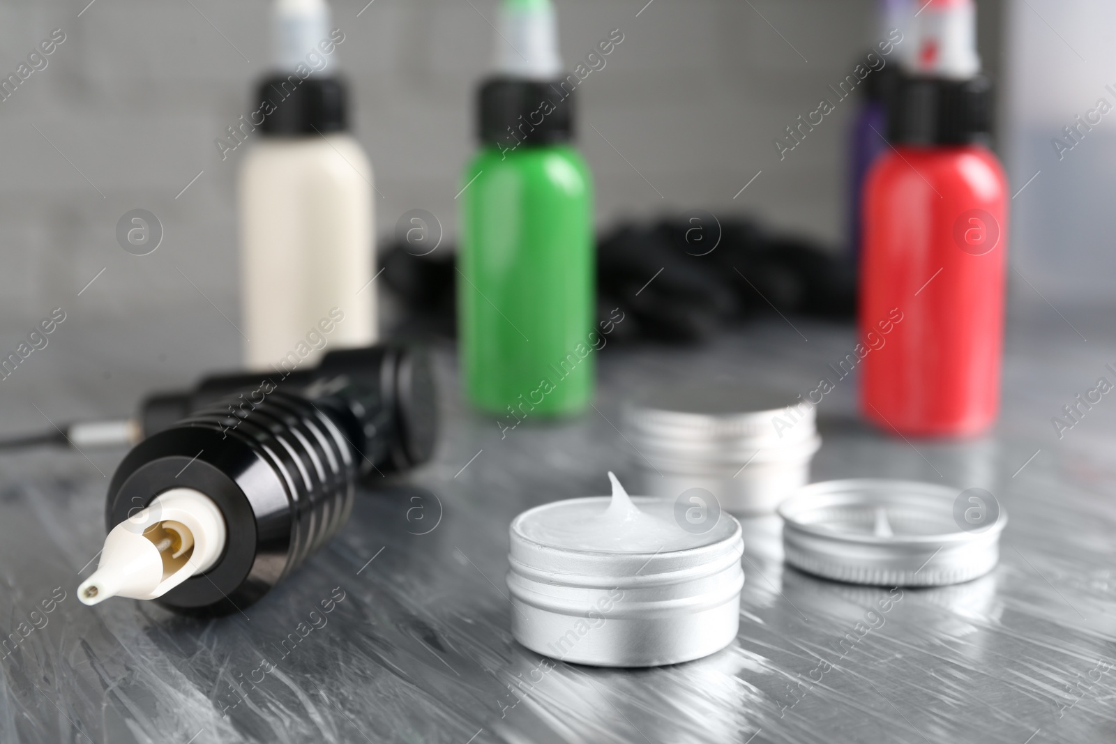 Photo of Modern professional tattoo machine and ointment on table in salon