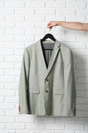 Photo of Woman holding hanger with grey jacket near white brick wall, closeup