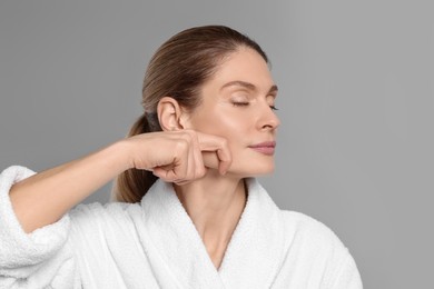 Photo of Woman massaging her face on grey background