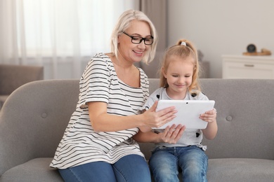 Photo of Portrait of mature woman and her granddaughter using tablet together in living room