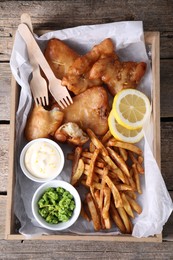 Photo of Tasty fish, chips, sauce and peas on wooden table, top view