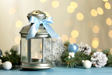 Photo of Christmas lantern with burning candle and festive decor on light blue wooden table against blurred lights