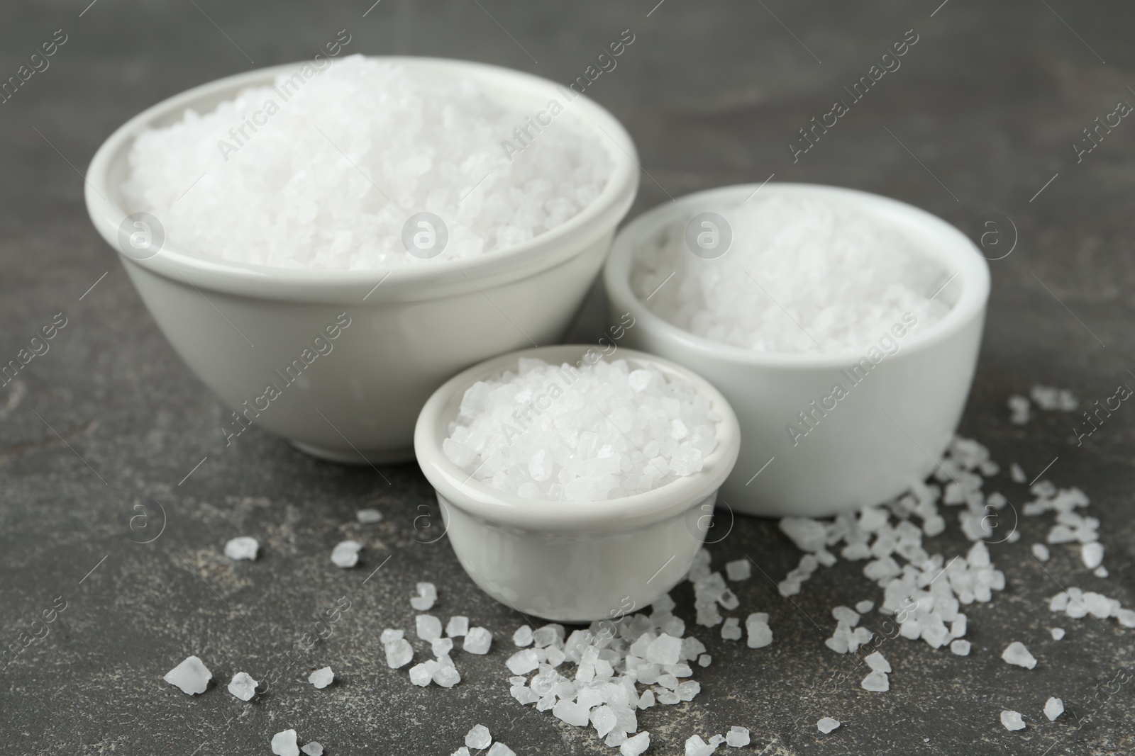 Photo of Bowls with natural sea salt on grey table