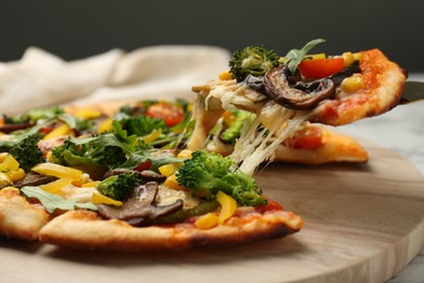 Photo of Taking piece of delicious vegetarian pizza at table, closeup