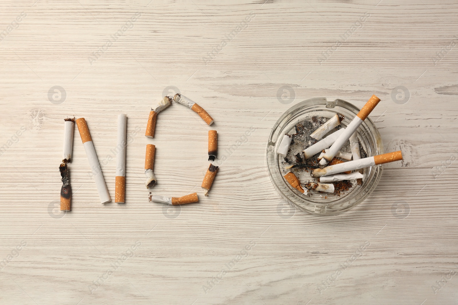 Photo of Word No made with burnt cigarettes and ashtray on white wooden table, flat lay. Stop smoking concept