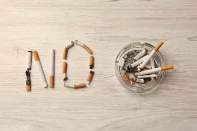 Photo of Word No made with burnt cigarettes and ashtray on white wooden table, flat lay. Stop smoking concept