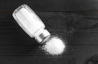 Organic salt in glass shaker on black wooden table, top view. Space for text