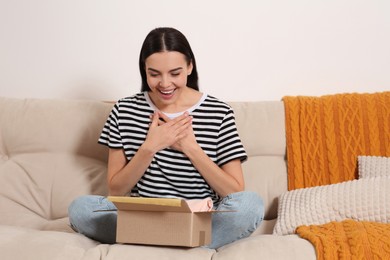 Photo of Emotional young woman with parcel on sofa at home. Internet shopping