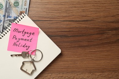 Photo of Note with words Mortgage Payment Holiday, key, notebook and money on wooden table, flat lay. Space for text