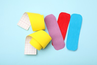 Photo of Bright kinesio tape pieces on light blue background, flat lay