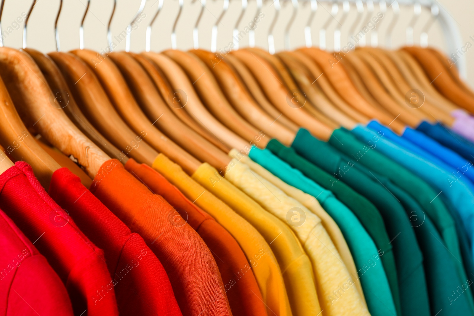 Photo of Rack with bright clothes on light background. Rainbow colors