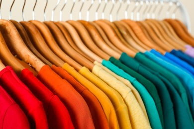 Photo of Rack with bright clothes on light background. Rainbow colors