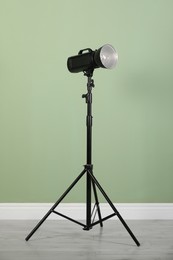 Studio flash light with reflector on tripod against pale green wall in room. Professional photographer's equipment
