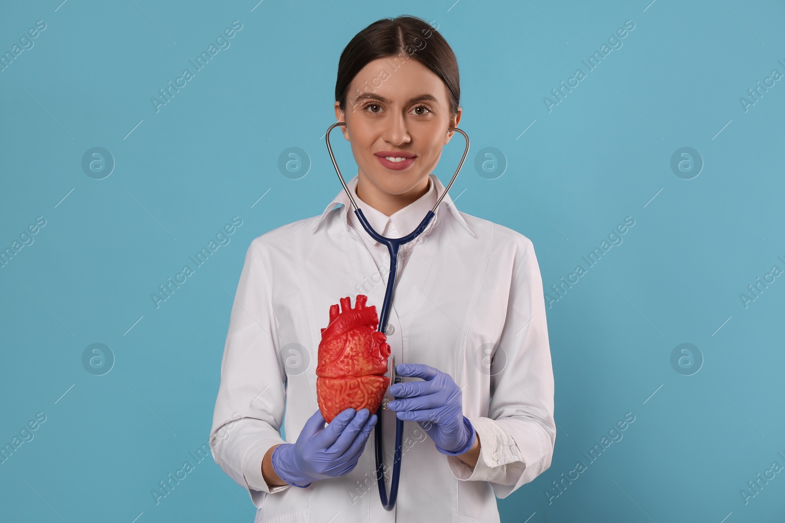 Photo of Doctor with stethoscope and model of heart on light blue background. Cardiology concept