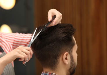 Photo of Barber making stylish haircut with professional scissors in beauty salon, closeup