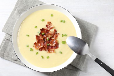 Tasty potato soup with bacon in bowl and spoon on white wooden table, top view