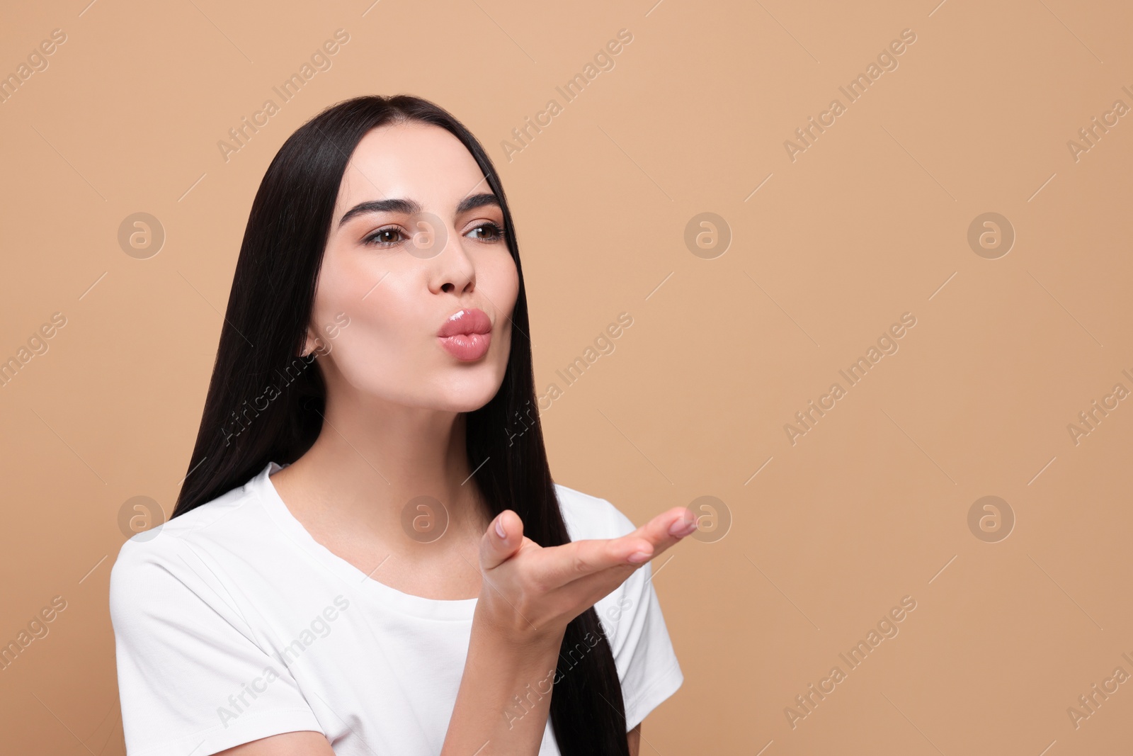 Photo of Beautiful young woman blowing kiss on beige background. Space for text