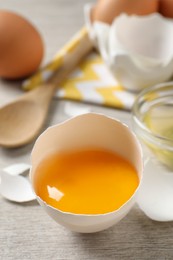 Photo of Cracked eggshell with raw yolk on white wooden table, closeup