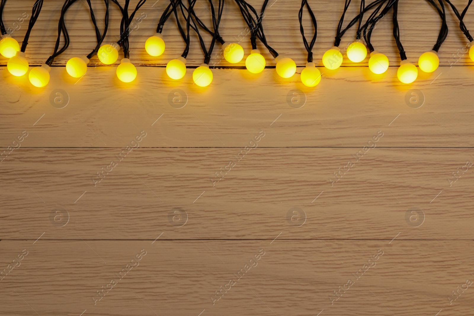 Photo of Glowing festive lights on wooden background, top view. Space for text