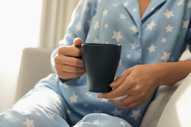 Woman in pajamas with cup sitting on sofa at home, closeup