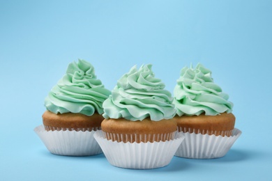 Tasty cupcakes with cream on light blue background