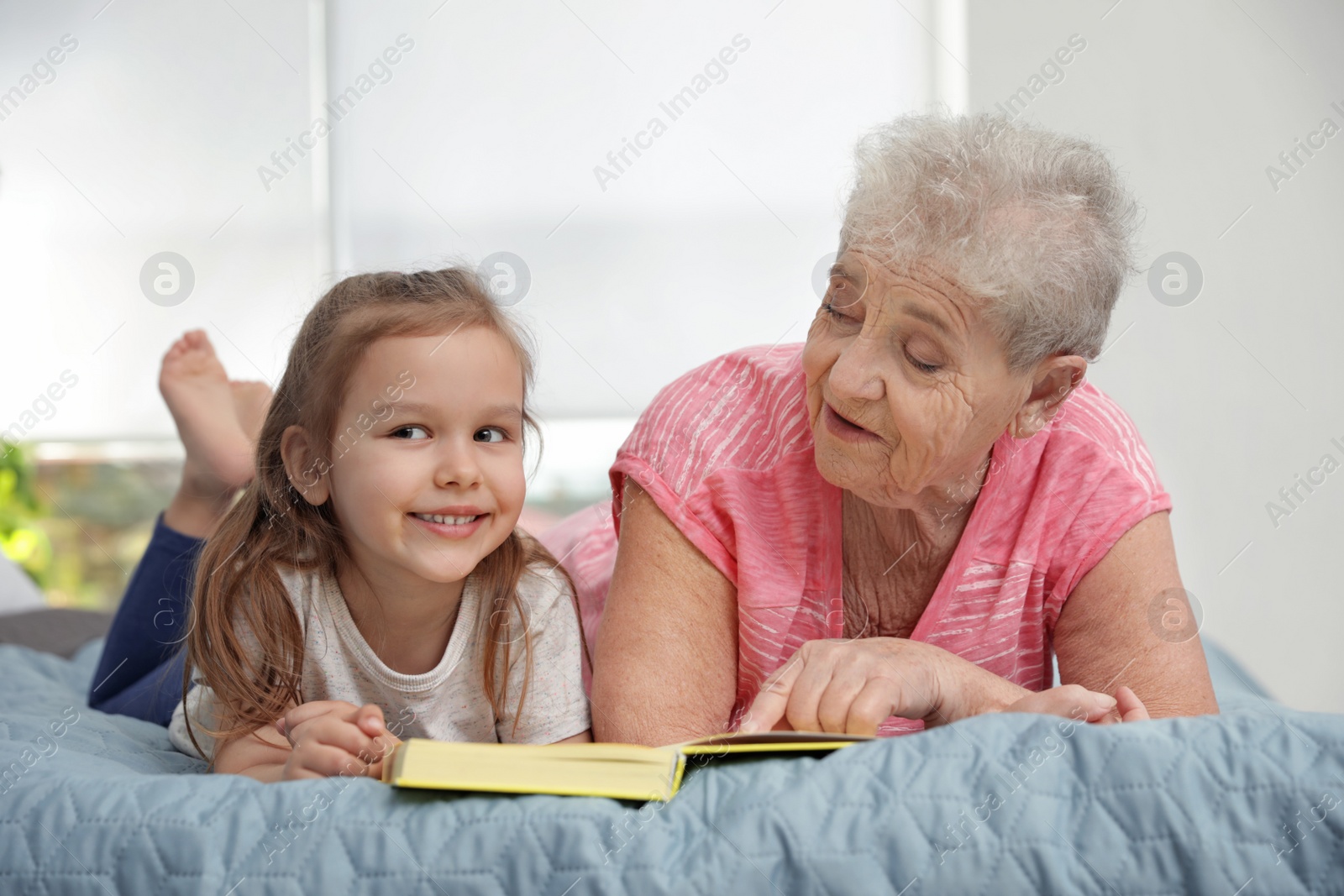 Photo of Cute girl and her grandmother reading book on bed at home