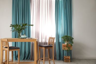 Photo of Stylish wooden table and chairs near window with elegant curtains in room