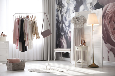 Photo of Rack with stylish women's clothes and handbag indoors. Interior design