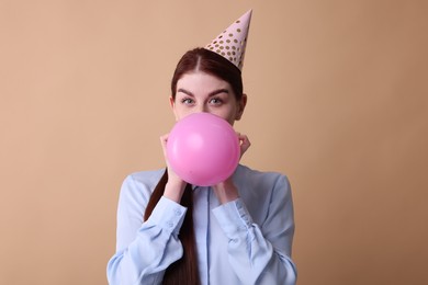 Photo of Young woman in party hat blowing balloon on beige background