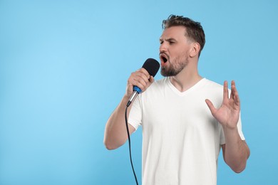 Handsome man with microphone singing on light blue background. Space for text