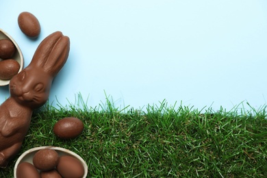 Photo of Chocolate Easter bunny and eggs with green grass on light blue background. Space for text