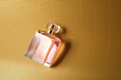 Photo of Luxury women's perfume. Sunlit glass bottle on golden surface, top view. Space for text