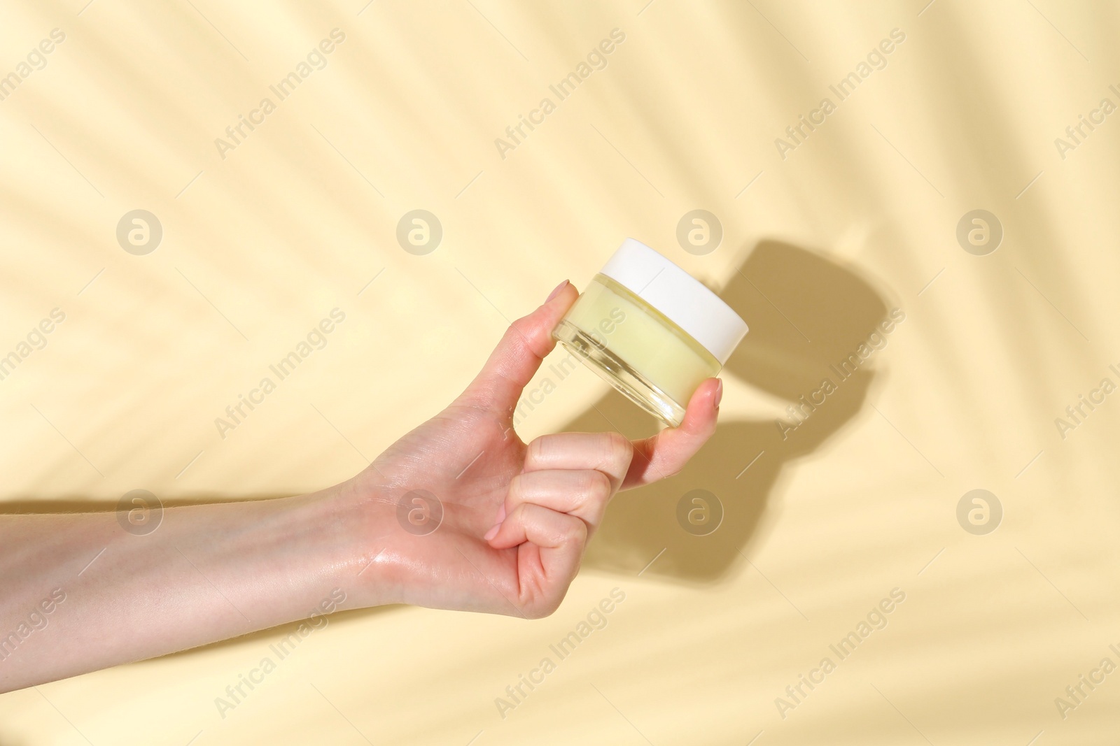 Photo of Woman holding jar of cream on yellow background, closeup