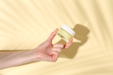 Woman holding jar of cream on yellow background, closeup